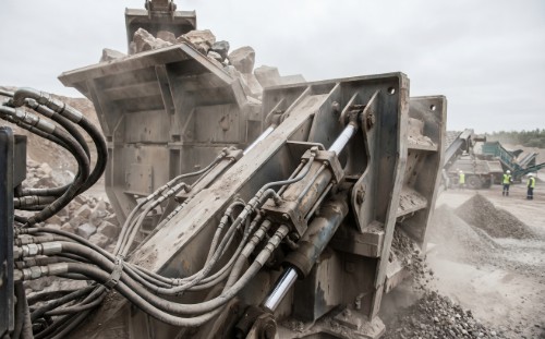 Large aggregate crusher in operation at a quarry with visible hydraulic cylinders and hose lines
