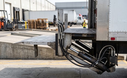 Commercial semi-truck with hydraulic lift gate cylinder and hose lines at a logistics depot