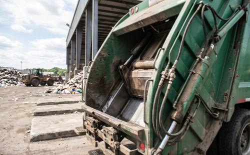 Waste collection truck with hydraulic ram cylinder extended at a waste facility